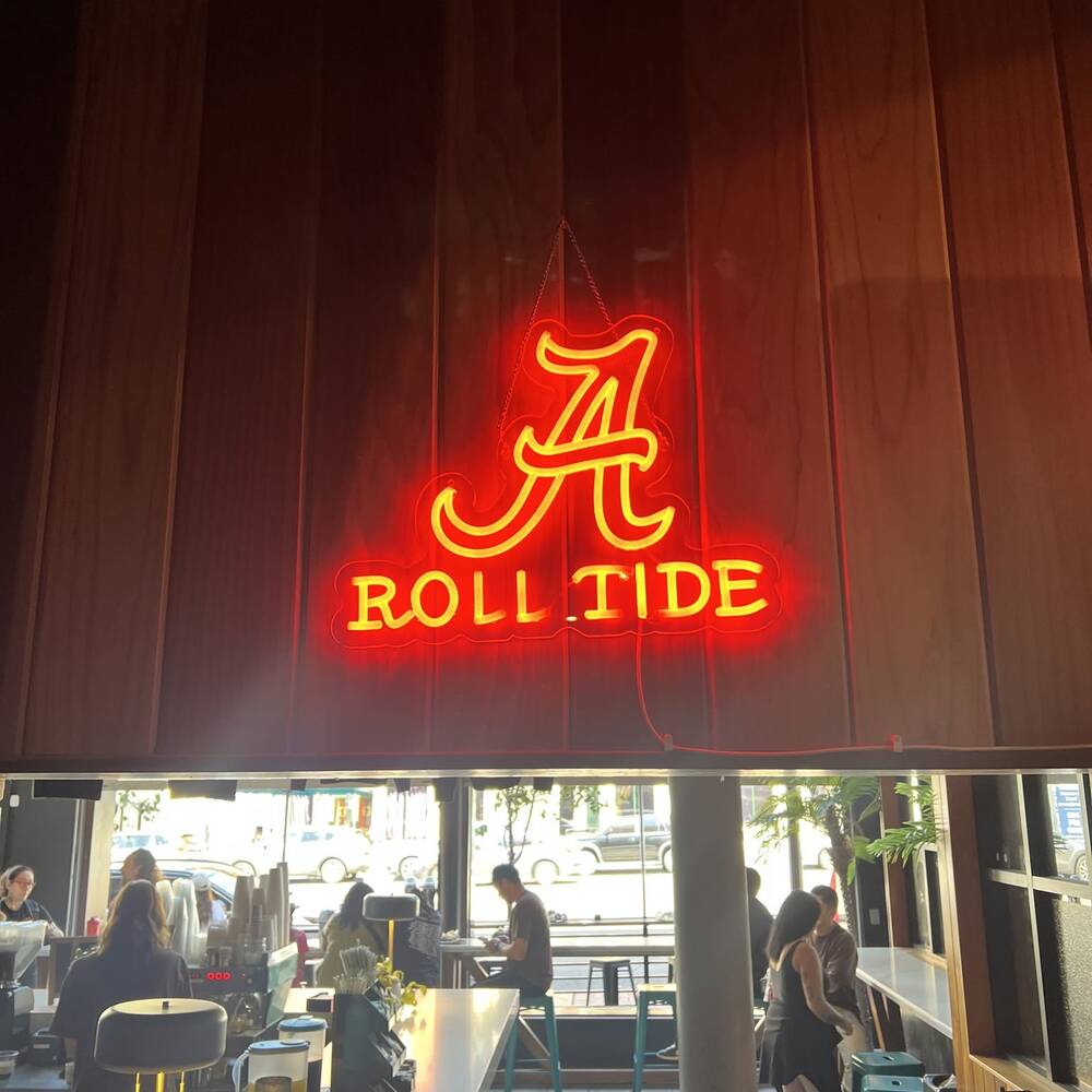 A neon Alabama script A and Roll Tide sign on the wall inside the bar