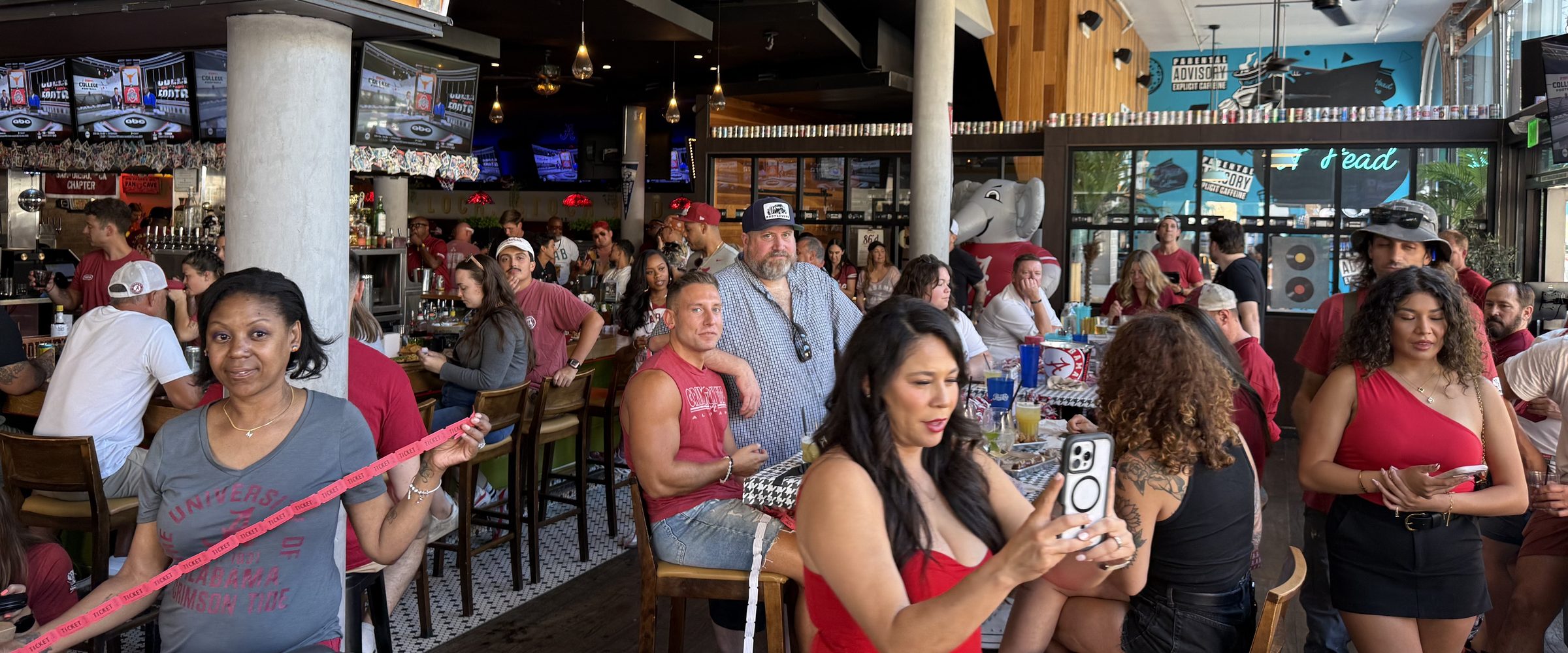 A packed room at The Smoking Gun on game day, fans in crimson at the bar and around the tables with the televisions on above them